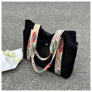 Close-up of black nylon tote bag featuring floral pattern strap and side pocket detail