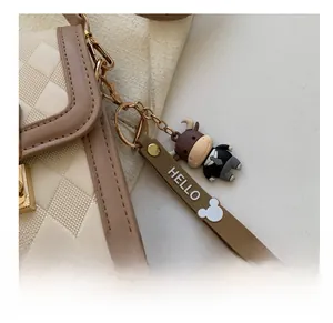 Detailansicht eines Cartoon-Kuh-Anhängers an einer beige gesteppten Tasche mit Goldkette