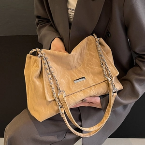 Brown pleated tote bag with silver chain straps and metallic logo plate shown on a model