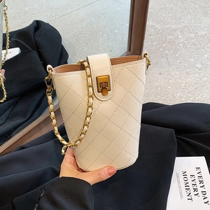 Elegant cream quilted bucket bag with gold chain strap held against black clothing