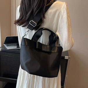 Women's black nylon bucket bag featuring a large decorative bow and wide shoulder strap