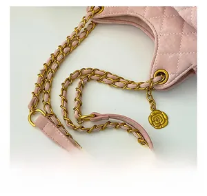 Détail d'un sac à main matelassé rose avec bandoulière dorée et pendentif camélia