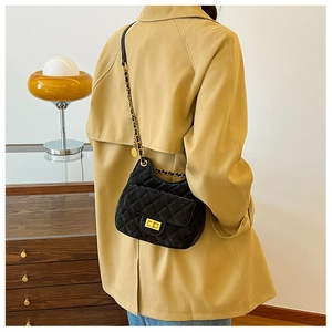 Sac bandoulière matelassé en velours noir avec chaîne dorée porté sur un manteau beige