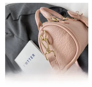 Nahaufnahme der rosa Zylindertasche mit Lederstruktur und goldenem Metallhaken-Detail