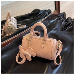 Detailansicht der rosa Zylindertasche mit Lychee-Narbenstruktur und Schmetterlings-Anhänger