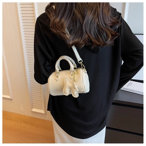 Weiße Zylindertasche mit Lychee-Textur und Elefantenanhänger an einem Modell gezeigt