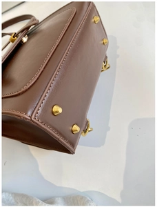 Detailed view of dark brown leather bag bottom with four protective gold metal feet studs