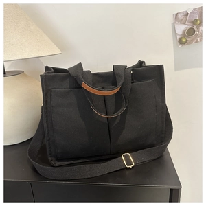 Detail of black canvas tote with leather handle accents and multiple front utility pockets