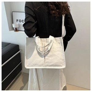 Detail of a beige canvas tote bag showing dual front pockets and detachable shoulder strap