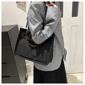 Detail of black canvas tote bag showing brown leather handles and functional front pocket