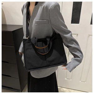 Detail of black canvas tote showing leather-wrapped handles and adjustable strap