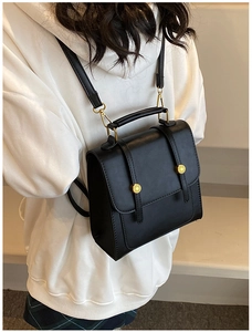 Model wearing a black leather backpack with gold buckles and dual shoulder strap design