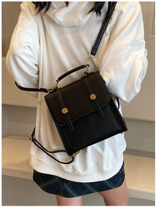 Detail of black pebbled leather backpack with gold buckles worn by a model in white