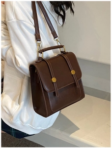Detail of dark brown faux leather vintage handbag with golden buckles and top handle