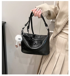 Detail of black oil-wax textured PU shoulder bag with cute white plush monster charm