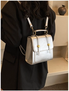 Close-up of a metallic silver mini backpack with gold hardware worn on a black blazer