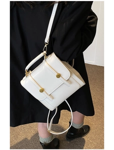 Detail of white faux leather bag featuring glossy finish and gold circular metal buckles
