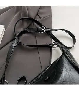 Close-up of black glossy pleated shoulder bag with silver hardware on a grey blazer