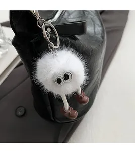 Close-up of white plush monster keychain with big eyes and brown shoes on black bag