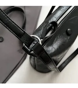 Close-up of black PU leather shoulder bag featuring silver metal rings and smooth zipper detail