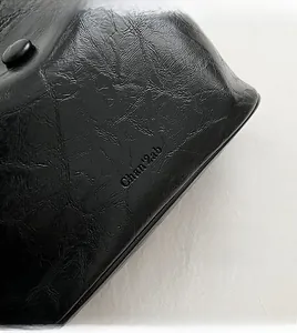Close-up of black pleated leather texture and embossed logo on a vintage bucket bag