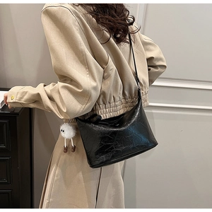 Detail of black pleated shoulder bag with white plush sheep charm on khaki jacket