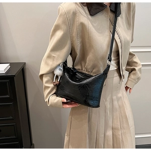 Close-up of black bucket bag with glossy texture and a white plush charm detail
