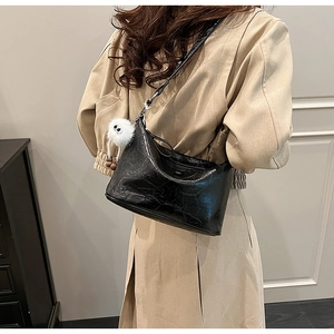 Detail of black glossy PU leather crossbody bag with white plush monster charm