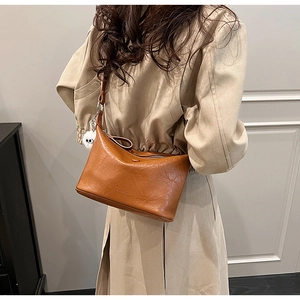 Close-up of caramel leather bucket bag featuring retro pleated texture and plush charm