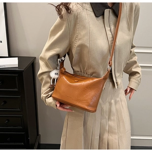 Detailed close-up of brown leather bucket bag with cute white plush monster keychain