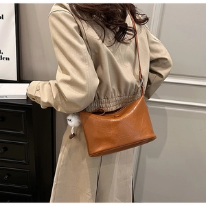 Close-up of brown vintage leather bucket bag with brand logo and white plush toy pendant