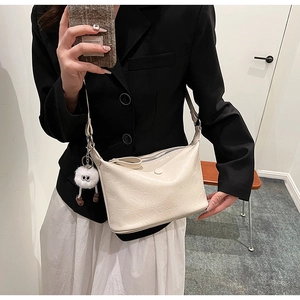 Close-up of off-white PU leather shoulder bag with plush charm and zipper detail