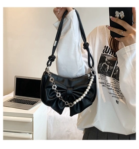 Detail of black leather bow bag featuring decorative pearl and metal floral chains