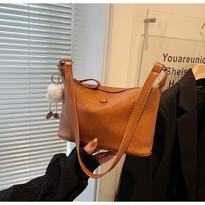 Detail of caramel oil wax leather bucket bag with textured finish and soft white fur charm
