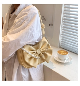 Detail of cream bow shoulder bag with pearl flower chain strap on model with white shirt