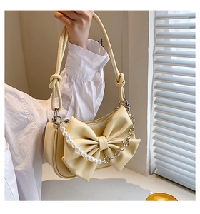 Close-up of cream bow handbag featuring pearl chain and floral metal detail