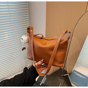 Detail of brown pleated leather bucket bag with a cute white plush monster keychain charm