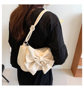 Detail of cream bow shoulder bag featuring pearl strap and floral metal chain accents