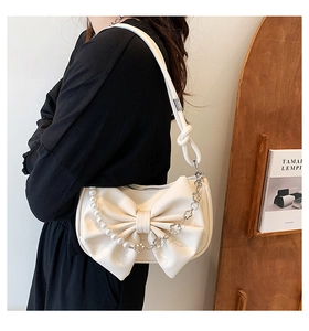 Detail of cream white bow shoulder bag with pearl accents and floral metal chains