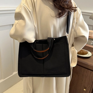 Black canvas tote bag with brown leather handles shown in a lifestyle crossbody view