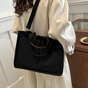 Black canvas tote bag with adjustable shoulder strap and leather trim in minimalist style