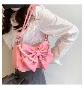 Pink bow shoulder bag with pearl chain detail shown on a model in a white outfit