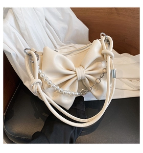 Detail of cream white faux leather shoulder bag featuring a large bow and pearl chain