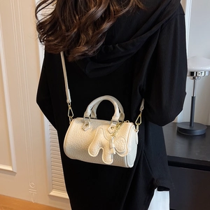 Schicke beige Zylindertasche mit goldenen Beschlägen und Anhänger auf schwarzem Outfit