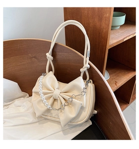 Close-up of ivory bow bag with decorative pearls and silver floral chain detailing