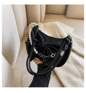 Detail of a black bow handbag with pearl and flower chain charm in glossy PU leather