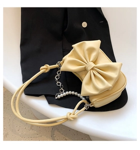 Detailed close-up of cream bow shoulder bag with pearl metal chain on black suit