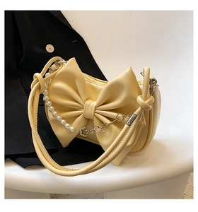 Detail of cream yellow shoulder bag featuring large bow, pearl chain and top zipper