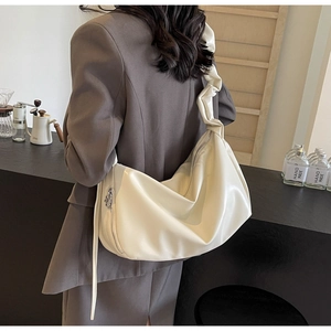 Détail de la bandoulière plissée crème et du pompon zippé argenté sur le sac croissant