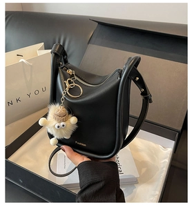 Detail of black leather bucket bag with gold zipper and plush charm in gift box